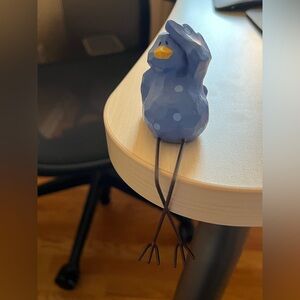 Russ clay and metal bird sculpture. It sits on the edge of a shelf/table